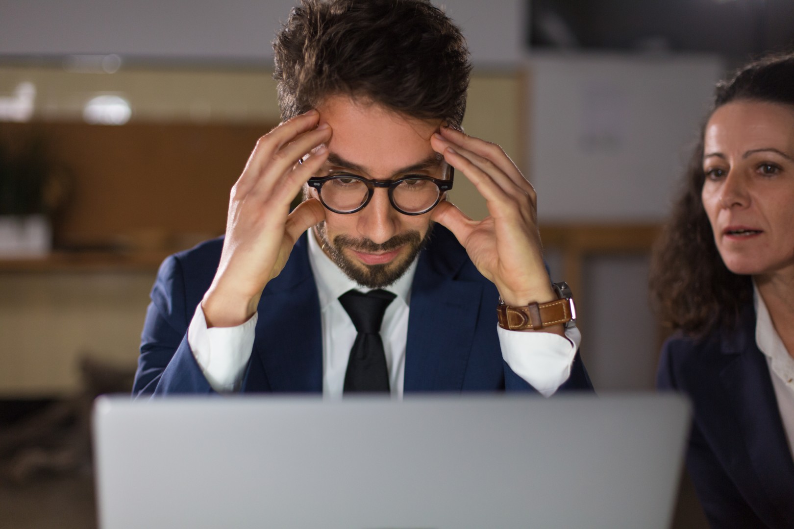 Front view of tired man in eyeglasses looking at laptop